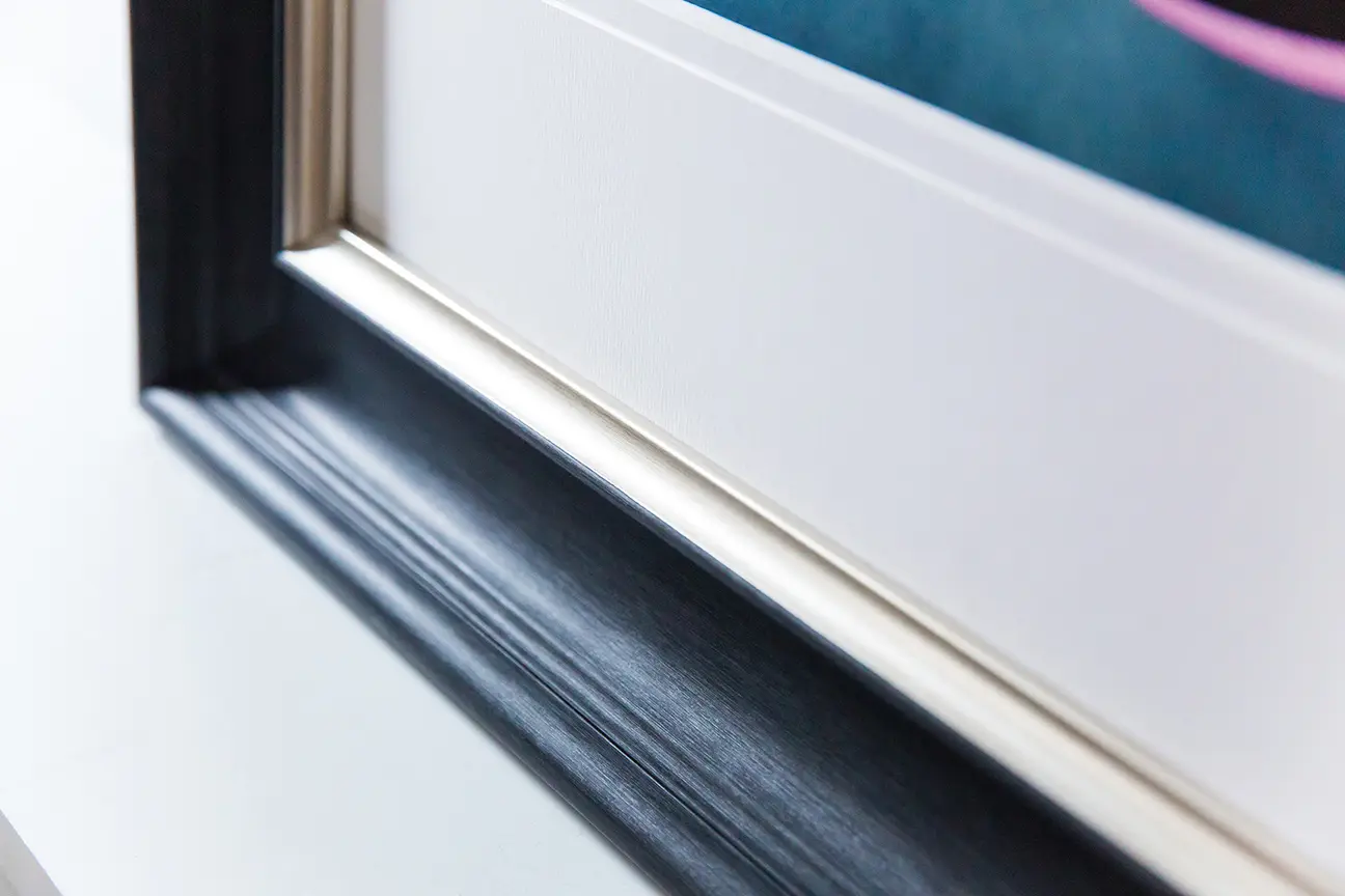Close-up of a polymer picture frame with a black, glossy outer edge and a white inner mount, focusing on the corner where the frame and mount meet.