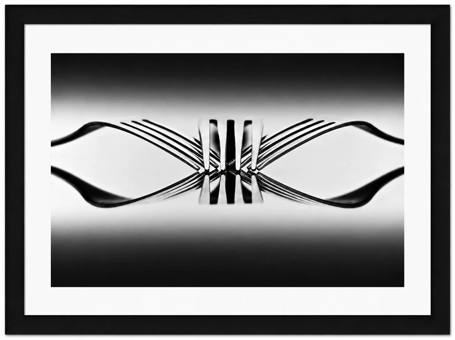 Black and white photo of four forks standing upright, their tines interlocked and reflected on a glossy surface, creating a symmetrical, abstract pattern. Presented as one of the elegant Noel Fenech Framed Prints with a white mount and black frame.