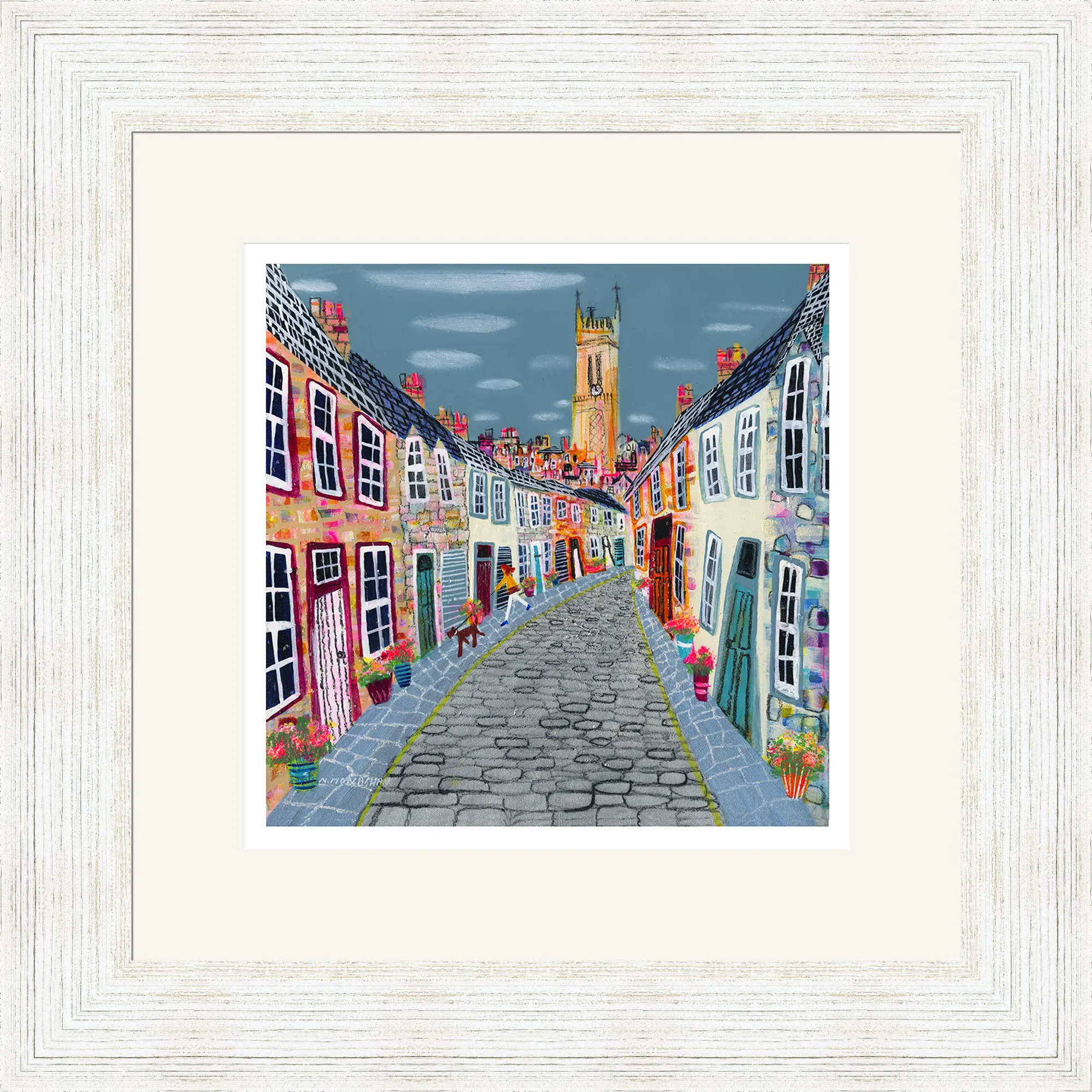Colourful painting of a cobbled street lined with bright houses, flower pots, and benches, leading to a tall church tower under a cloudy sky. White wooden frame surrounds the artwork.