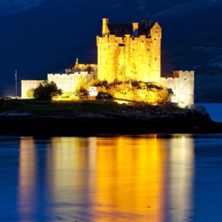 Eilean Donan Castle illuminated at night, reflecting on Loch Duich in a portrait-oriented photograph