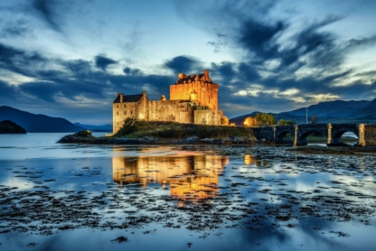 Eilean Donan Castle illuminated during blue hour after sunset, reflecting on calm waters