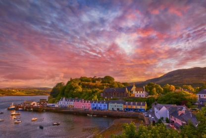 • Sunset over famous Quay Street in Portree, Isle of Skye, with golden hues and tranquil waters